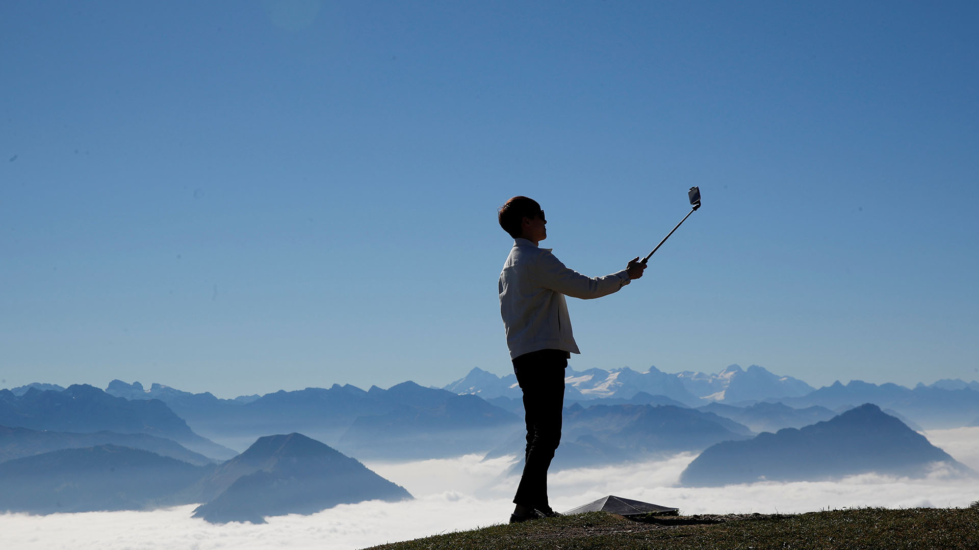 A man takes a picture with his smartphone mounted on a selfie stick during sunny autumn weather near the peak of Mount Rigi