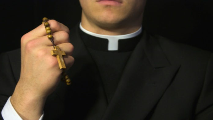 Young Priest praying with rosery in his hand