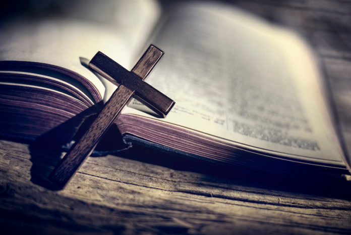 Praying with wooden crucifix cross on Holy Bible background